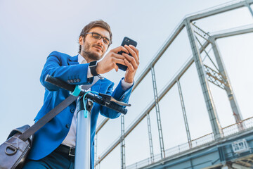 Low angle view of business man using mobile phone on electric scooter on city street near bridge....