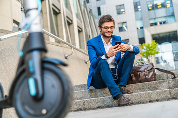 Handsome young businessman sitting on stairs using phone near electric scooter. Manager ceo lawyer...