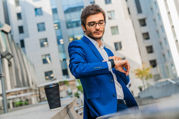 Portrait of young man in suit looking at watch on wrist for meeting. Handsome businessman waiting...