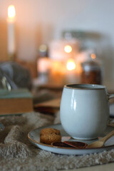 Cup of tea or coffee, cookies, books, glasses, e-reader, almonds, ball of yarn, knitting needles and lit candles on the table. Hygge at home. Selective focus.