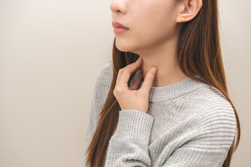 Sickness in inflaming asian young woman, girl use hand check self touch at sore throat, pain thyroid gland on neck or disease reflux, acid of suffer people on wall background. Medical and healthcare. - obrazy, fototapety, plakaty