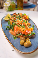 salmon with lemon, olives and microgreens on a blue plate on the table