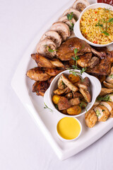 Top view Assorted roasted meats, colorful vegetables, and golden potatoes garnished with fresh parsley and savory sauces on a white platter
