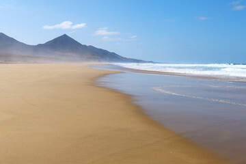 Fototapeta na wymiar Menschenleerer Strand von Cofete mit Dunst und Wellen und Sonnenschein