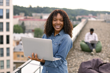 Attractive African American female freelancer using portable computer for remote work at roof top...