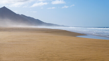 Menschenleerer Strand von Cofete mit Dunst und Wellen und Sonnenschein