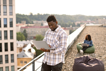 Successful business man dressed in checkered shirt standing on roof top outdoors and typing on...