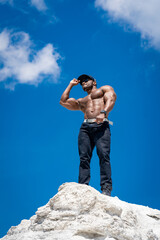 Muscular man stands on rock and looks into the distance, Muscular man stands on rock and looks into...