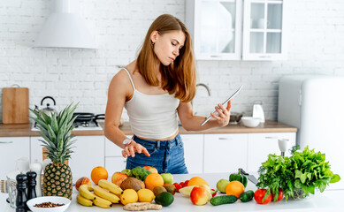 Young woman standing in the kitchen with tablet computer and using mobile phone for shopping online, Young woman standing in the kitchen with tablet computer and using mobile phone for shopping online