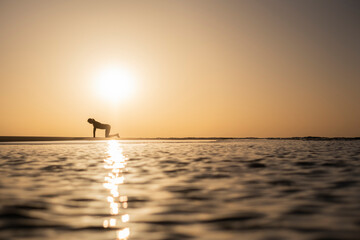 Mujer practicando yoga a la salida del sol en la orilla del Océano