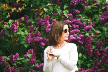 Spring portrait of pretty mature woman posing with lilac flowers on background - 745993602