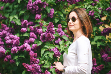 Spring portrait of pretty mature woman posing with lilac flowers on background - 745993603