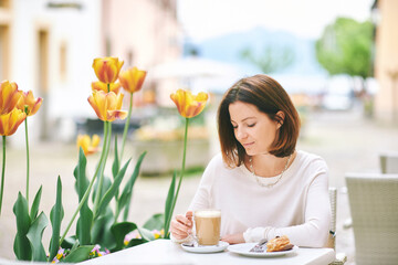 Portrait of happy mature woman having coffee with croissant in outdoor cafe - 745993673