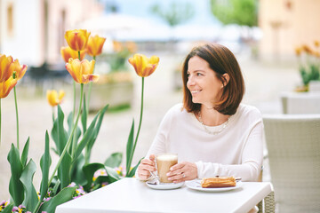 Portrait of happy mature woman having coffee with croissant in outdoor cafe - 745993678