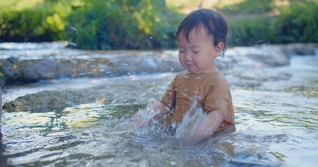 Fototapeta premium Exuberant toddler splashing in a shallow stream, laughter sparkling as sunlight filters through green foliage in a blissful outdoor scene