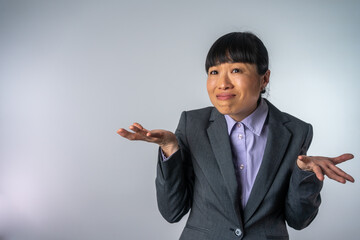 Young pretty Asian business woman looking sideways with doubtful and skeptical expression. Businesswoman making a face isolated on grey background. Woman doubting on a grey background