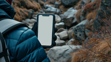 A male traveler in the mountains holds a phone with a white screen. - obrazy, fototapety, plakaty
