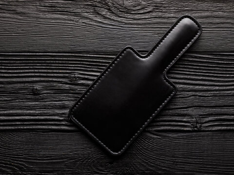 adult toy for sex over black wooden background. bdsm latex paddle for spanking