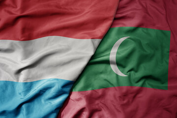 big waving national colorful flag of maldives and national flag of luxembourg .