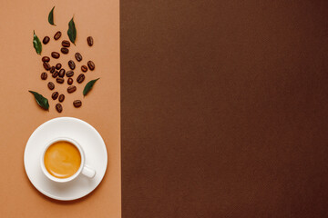 Cup of espresso coffee with coffee beans and leaves on cream and brown background with copy space.