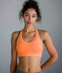 Fototapeta na wymiar Attractive, strong and young sports woman with a sports bra posing after workout showing strong, sporty and slim body: Athletic young mixed-race woman with curly hair in an orange sports bra.