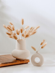 Elegant vase set with dry bouquet flowers with sunlight shadows on white table, home interior...