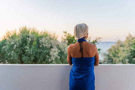 Unrecognizable woman from behind enjoying beautiful views of the Aegean sea from the terrace of her hotel at sunset from the Greek island of Crete