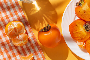 Creative layout made of fresh persimmon fruits and orange tangerin on bright background with ...