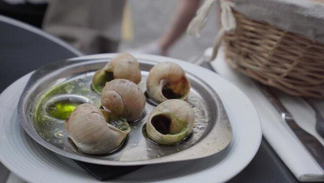 these are the famous escargots, a delicious French dish. In the shot you can see 6 pieces and with tongs a person takes one and brings it to his plate.
