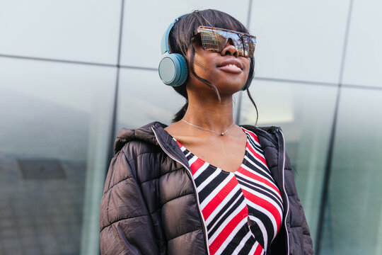 A trendy woman enjoys her music on the go, her stylish outfit harmonizing with the city's modern backdrop