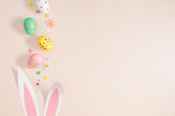 Easter holiday composition. Easter decorations, colorful eggs, funny bunny ears, sprinkles sugar candies on isolated pastel beige background. Easter concept. Flat lay, top view, copy space