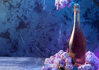 Champagne or cider bottle on a blue table, blooming purple lilac. Spring composition, copy space