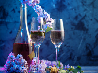 Two glasses and a bottle of champagne on a blue background with blooming lilac branches. Romantic spring evening