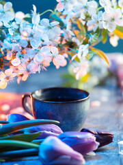 Coffee cup on the table with a bouquet of tulips and a branch of blooming white cherry. Spring composition.