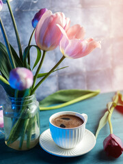 white ceramic cup of fragrant coffee on the table, a bouquet of pink tulips in a vase. blue background