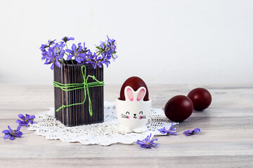 Easter card: a bouquet of blue flowers, painted eggs and white bunnies on the table, space for text