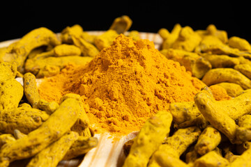 Turmeric powder and dried turmeric root on a black background