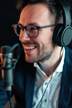 Focused male podcaster with stylish glasses and headphones speaks into a studio microphone, image rendered by generative AI