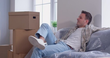 Man enjoys moving new apartment, new sofa sitting, cardboard carrying, excited homebuyer transporting boxes, organizing new home move, changing residence for better, male independence, life beginning