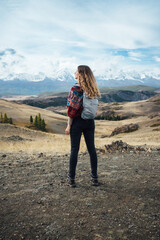 A traveler stands in awe, gazing at a breathtaking mountain vista, with the vastness of the landscape stretching out before her. Her backpack and attire suggest a journey into the wild. Adventurer