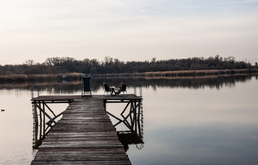 Young couple sitting on a pier in a sunset by lake. 