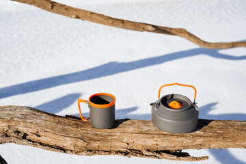 a cup and a kettle are sitting on a branch in the snow
