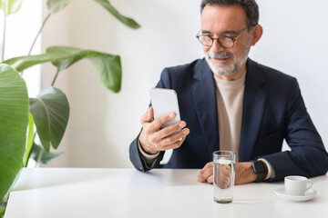 Engaged businessman in a modern workspace using a smartphone, with a glass of water and espresso