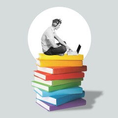 A man holds laptop sits on huge stack books.