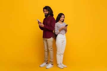 Indian man and woman standing back to back, using smartphone