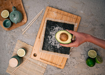 Nori seaweed with rice grains, avocado in a hand, chopsticks, fresh lime, green teacup on a modern...