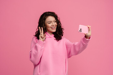 happy smiling woman in pink hoodie posing on pink studio background holding smartphone