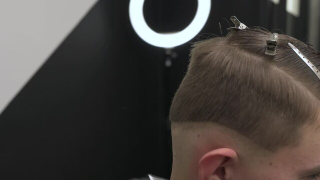 Barber shaves the temple with cordless trimmer during a short haircut on the sides of the head.