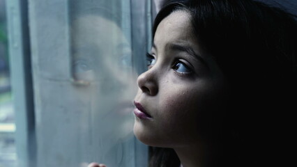 One depressed child leaning on glass window feeling sad and lonely at home, one small introspective...