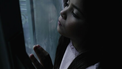 Lonely child feeling sad and depressed in moody winter scene by glass window. One thoughtful little...